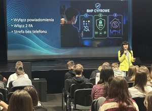 Na ekranie widoczny jest slajd z hasłem „BHP CYFROWE” oraz zaleceniami. W sali siedzą uczniowie uczestniczący w szkoleniu.
