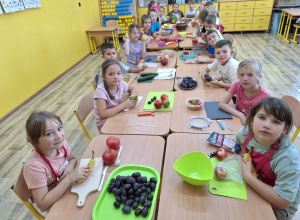 Uczniowie rozmawiają przy stoliku na temat warzyw i owoców.