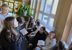 Jedna z uczennic czyta o tym, jak powstała książka. Grupa uczniów słucha czytanego przez uczennicę tekstu.