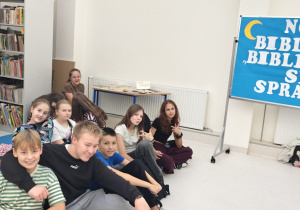 Uczniowie siedzą na materacach w bibliotece szkolnej podczas gry w ,,Kalambury finansowe”.