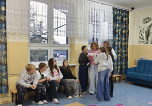 Uczniowie odczytują polecenie w języku angielskim. Pięcioro uczniów stoi. Czworo siedzi na ławeczce.