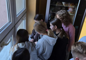 Uczniowie rozszyfrowują kod. Stoją na korytarzu przy oknie.
