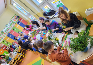 Rodzice i dzieci w grupie Pszczółki wykonują palmę wielkanocną.