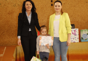 na zdjęciu znajdują się dwie dorosłe kobiety i jedno dziecko z dyplomem w ręku