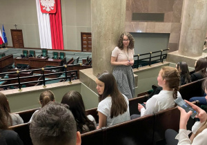 Zadowoleni uczniowie wysłuchują przewodniczki, która opowiada o początkach sejmu.