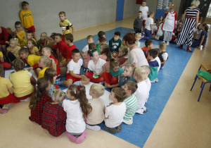 zdjęcie ukazuje grupę siedzących na korytarzu szkolnym dzieci wraz z nauczycielem, które pracują nad brystolem