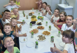 Uśmiechnięci uczniowie siedzą przy stole, na którym znajduje się słodko – owocowy poczęstunek.