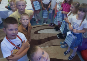 Uczniowie stoją w dwóch rzędach. Po prawej stronie dziewczynki trzymające prezenty, a po lewej stoją chłopcy.