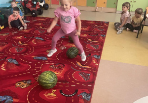 Dziewczynka z grupy Motylki w ogrodniczkach skacze nad arbuzem