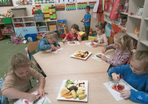 Dzieci 5 – 6 letnie zajadają ze smakiem zgromadzone w sali owoce.