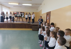 Kierownik szkoły dziękuje uczniom klasy 6 oraz wychowawczyni za przygotowanie części artystycznej. Na scenie uczniowie klasy 6, w tle tablica z dekoracją. Przed sceną po prawej stronie uczniowie klasy 1 i 2.