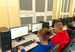 Pracownia komputerowa. Trzech chłopców projektuje swoje imienne breloczki. Zaprojektowane modele widoczne są na pulpicie ekranu.