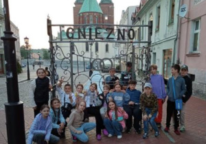 grupa uczniów na ławeczce z napisem Gniezno na tle Katedry Gnieźnieńskiej