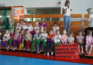 Dzieci siedzące na trybunach w kolorowych strojach, kibicują swoim kolegom