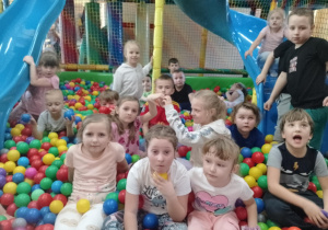 Dziewczynki i chłopcy z przedszkola w Rzeczycy siedzą na kolorowych piłeczkach w sali zabaw Kajtek.