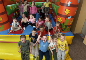 Zdjęcie grupowe dzieci z grupy Misie na tle kolorowej trampoliny w sali zabaw Kajtek.