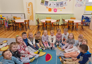Grupa dzieci z grupy ,,Pszczółki" siedzi na dywanie. Dzieci mają założone dwie różne kolorowe skarpetki.