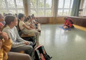 Uczniowie obserwują jak koleżanka z klasy VI pod okiem ratownika udziela pomocy poszkodowanemu.