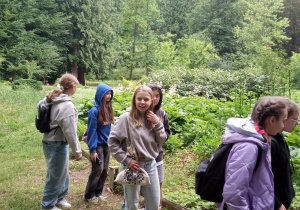 Uczennice spacerują ścieżkami arboretum za nimi wysokie drzewa.