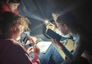 Uczennice pracują nad odczytaniem hasła-polecenia według podanego kodu. Jest ciemno. Mają włączoną latarkę w telefonie.