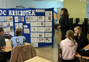 Nauczyciel bibliotekarz z biblioteki szkolnej opowiada uczniom dlaczego sławni ludzie czytają więcej. Na wystawce znajdują się zdjęcia sławnych ludzi, o których opowiada. Przedstawia uczniom również historię pisma i książki.