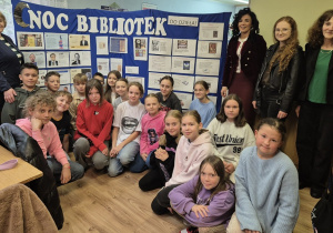Rozpoczęcie Nocy Bibliotek w Bibliotece Szkoły Podstawowej w Rzeczycy. Pani Dyrektor SP w Rzeczycy, pani Dyrektor GOK w Rzeczycy, pani polonistka i nauczyciel biblioteki szkolnej oraz uczniowie znajdują się na tle tablicy z historią pisma i książki oraz wystawki pt. ,,Dlaczego ludzie sławni czytają więcej?”