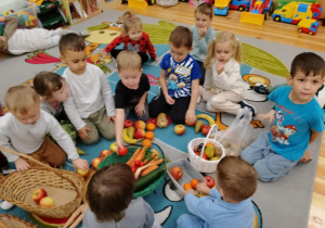 Dzieci z grupy Kamyczki w czasie zajęć edukacyjnych oglądają, dotykają i wąchają przyniesione owoce i warzywa.