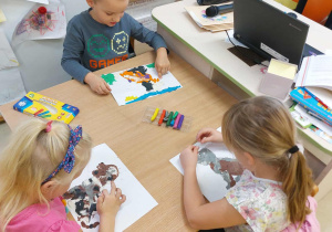 Dwie dziewczynki i chłopiec z grupy Zuchy wyklejają pieska plasteliną.