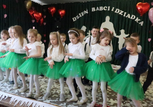 Dziewczynki w zielonych spódniczkach tańczą.