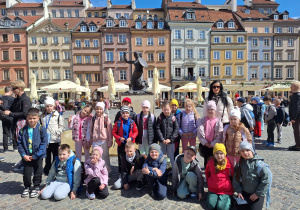 Uczniowie klasy pierwszej z Sadykierza znajdują się na Rynku Starego Miasta i pozują do zdjęcia przed Syrenką Warszawską.