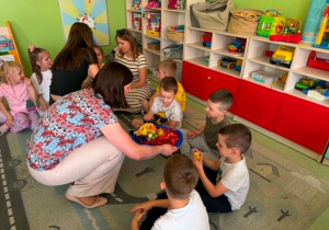 Psycholog oraz Pedagog specjalny rozdaje owoce dzieciom.