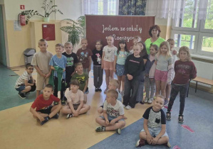 Uczniowie klasy I z panią Mariolą Kraszewską na wspólnej fotografii na tle tablicy z napisem „Jestem ze szkoły w Rzeczycy”.