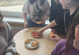 Uczniowie degustują gofry z owocami.