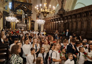 Społeczność szkolna, zaproszeni goście oraz laureaci podczas uroczystego podsumowania konkursu w murach katedry. W tle widoczne są monumentalne, rzeźbione z ciemnego drewna stalle, zabytkowy żyrandol oraz błyszczący, złocony ołtarz.