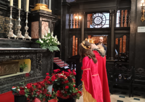 Wnętrze zabytkowej kaplicy wykonanej z ciemnego marmuru i drewna. Symboliczny pokłon postaci wcielających się w rolę historycznych patronów konkursu przed ołtarzem św. Jadwigi w katedrze na Wawelu.