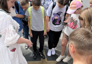 Grupa uczniów z przewodniczką przygląda się wmurowanej w chodnik mosiężnej gwieździe w Łódzkiej Alei Gwiazd na ulicy Piotrkowskiej.