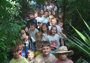Grupa uczniów na schodach w palmiarni, otoczona gęstą, tropikalną roślinnością.