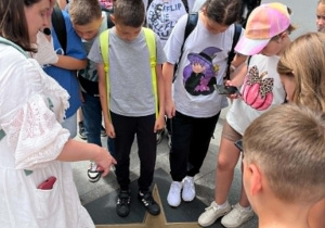Grupa uczniów z przewodniczką przygląda się wmurowanej w chodnik mosiężnej gwieździe w Łódzkiej Alei Gwiazd na ulicy Piotrkowskiej.
