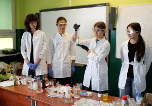 Uczennica , która trzyma cylinder laboratoryjny z wynikiem doświadczenia.