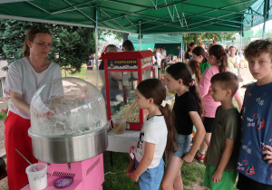 Stoisko z watą cukrową i popcornem w otoczeniu dzieci.