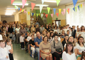 Uczniowie, rodzice i nauczyciele zgromadzeni na korytarzu szkolnym podczas inauguracji roku szkolnego.