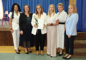Pani Katarzyna Zabielska trzyma kwiaty, stojąc w otoczeniu dyrekcji szkoły oraz zaproszonych gości.