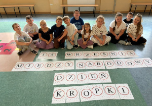 Uczniowie klasy 3 prezentują swoje ubrania w kropki siedzą przed napisem: 15 – sty Września Międzynarodowy Dzień Kropki.