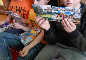 Od lewej: Kacper Heleniak, Kuba Woźniakowski i Kacper Kania. Chłopcy siedzą na materacu i z ciekawością czytają otrzymane pocztówki.