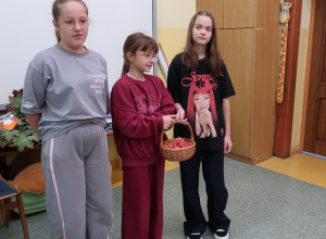 Trzy uczennice z samorządu stoją w klasie z wiklinowym koszykiem pełnym cukierków na Dzień Przedszkolaka.