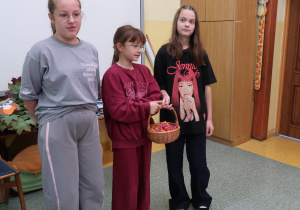 Trzy uczennice z samorządu stoją w klasie z wiklinowym koszykiem pełnym cukierków na Dzień Przedszkolaka.
