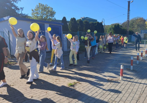 Uczniowie idą i podnoszą balon do góry.
