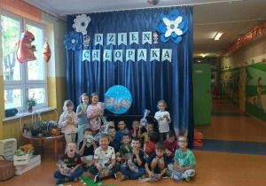 Grupa „Mądre Sówki” prezentu na tle dekoracji z okazji Dnia Chłopaka.