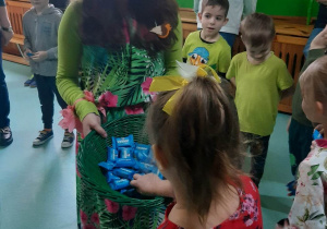 Pani Wiosna Madzia częstuje dzieci cukierkami z zielonego koszyka.
