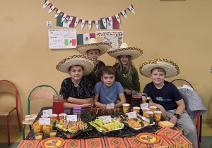 Uczniowie 4 klasy w kapeluszach sombrero przy stoisku z potrawami i dekoracjami Meksyku.